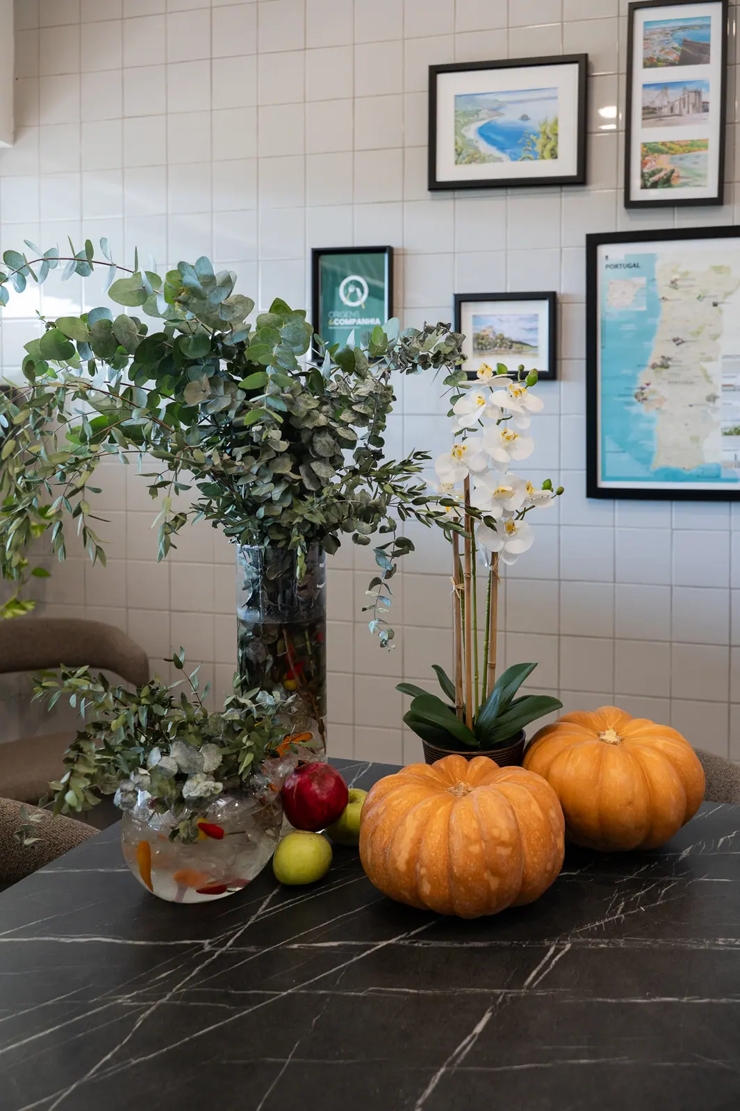 Eucalyptus, orchid and pumpkins on a table with framed Portugal prints