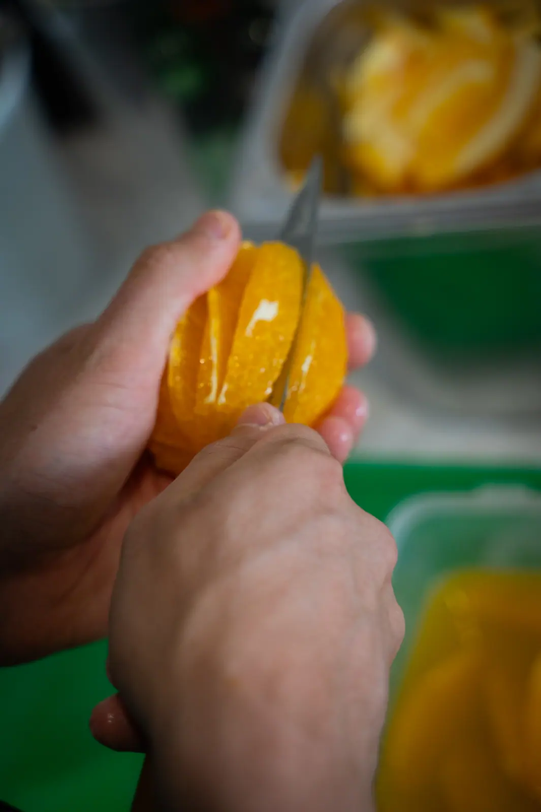 Hands cutting orange segments with a knife