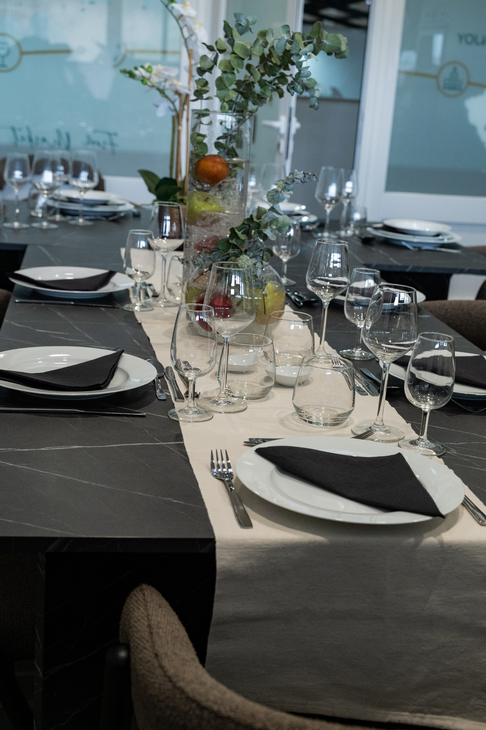 Mesa posta com copos, pratos e centro de mesa com eucalipto e fruta